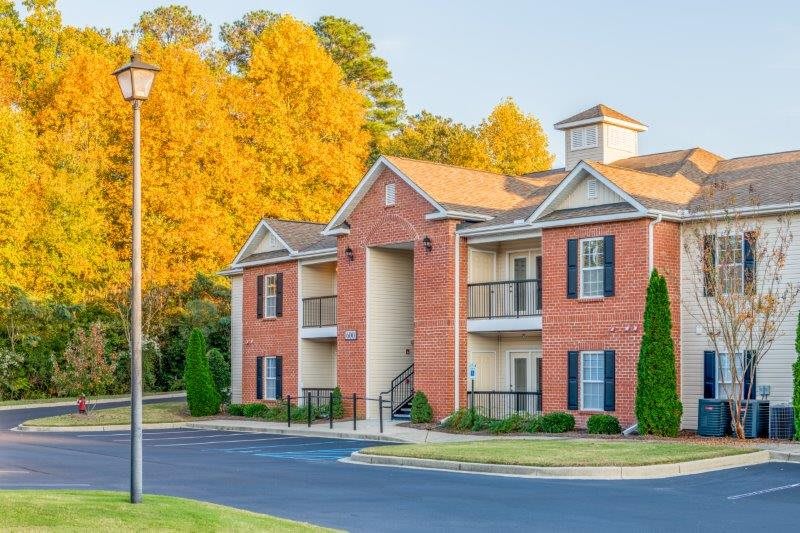 A suburban apartment building with a brick exterior and balconies, surrounded by autumn foliage.