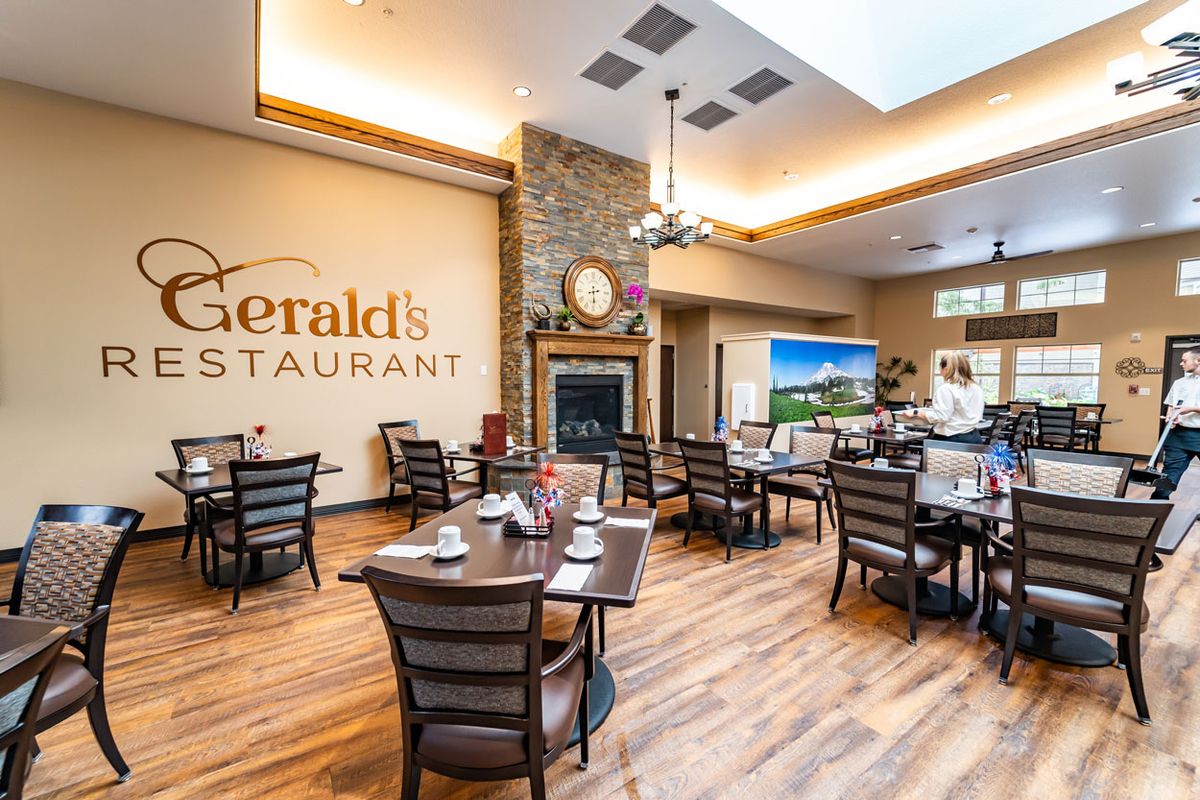 A cozy restaurant interior with neatly arranged tables and chairs, featuring a fireplace and warm lighting.