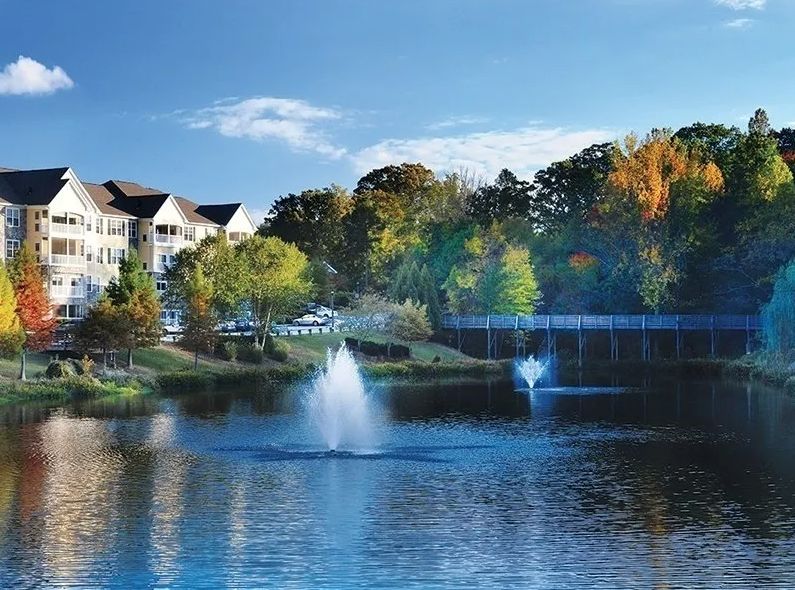A tranquil lake with fountains, surrounded by trees and buildings.