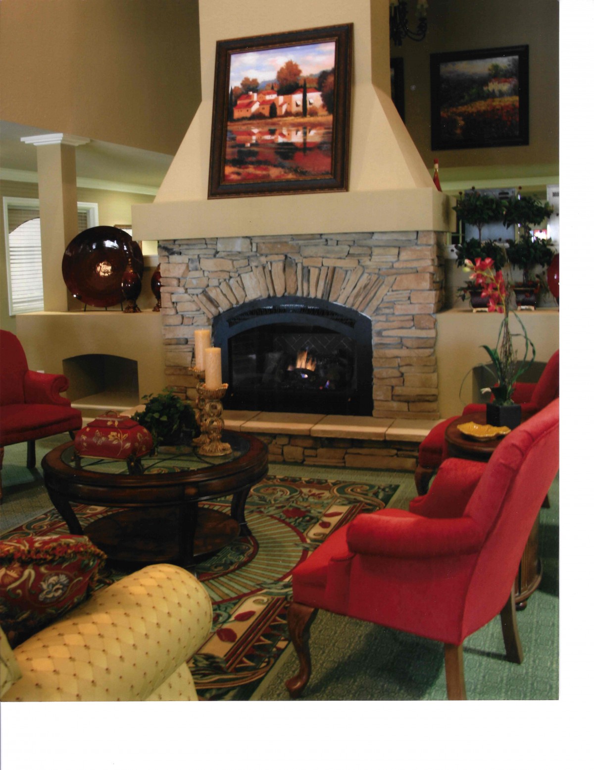 A cozy living room with a stone fireplace surrounded by red chairs and warm decor.