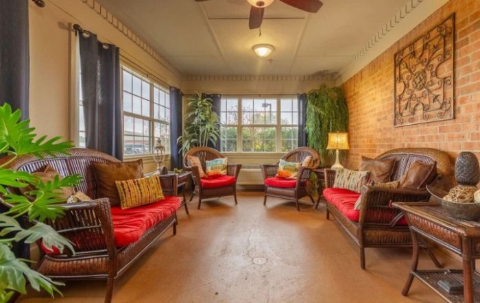 A cozy living room with wicker furniture, bright red cushions, and large windows letting in natural light.