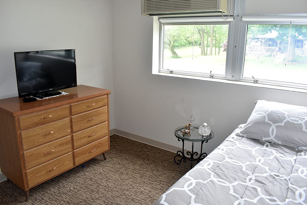 A cozy bedroom with a dresser, TV, and side table next to the bed.