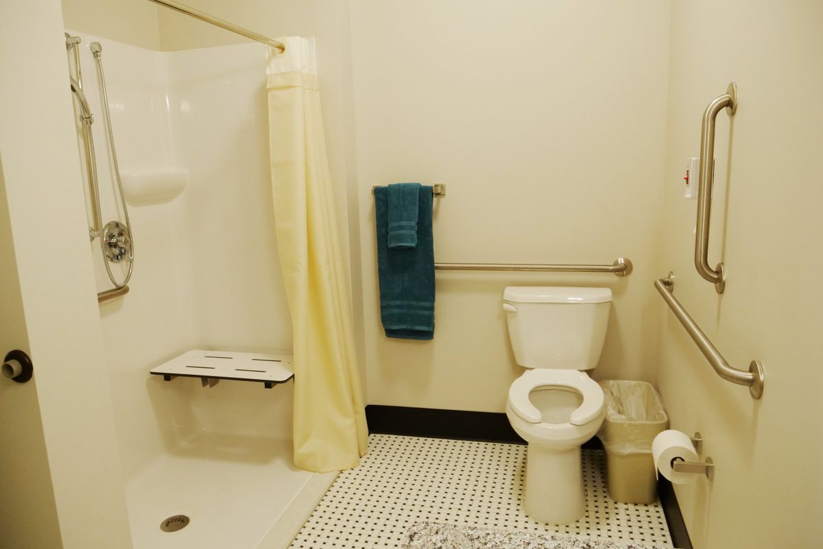 An accessible bathroom featuring a shower with grab bars, a toilet, and a towel on the wall.