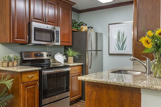 A modern kitchen featuring stainless steel appliances, wood cabinets, and a granite countertop.
