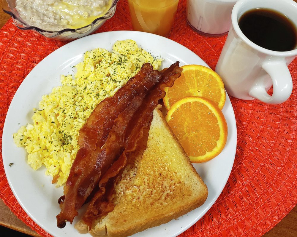 A classic breakfast with scrambled eggs, crispy bacon, toast, orange slices, and a cup of coffee.