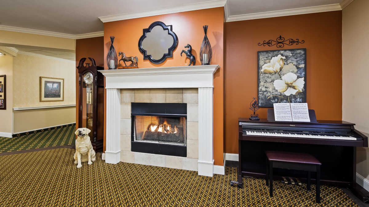 A cozy living room with a fireplace and a piano, featuring warm decor and artwork.