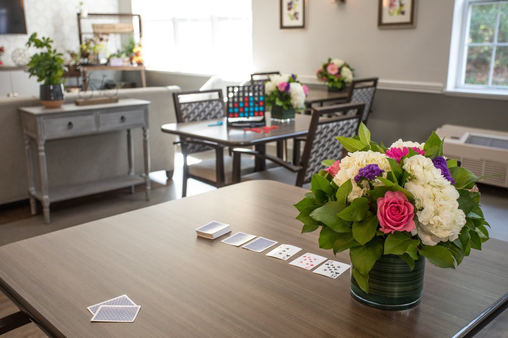 A cozy room with a table adorned with flowers and playing cards, surrounded by chairs.