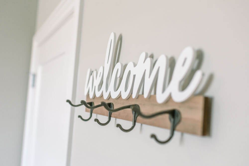 A decorative welcome sign with coat hooks in an entryway.
