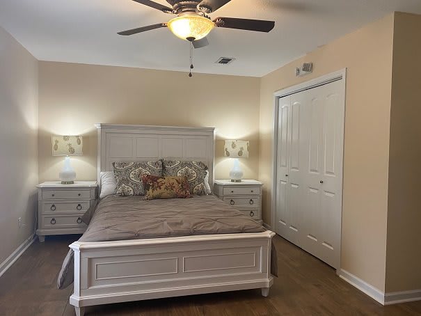 A cozy bedroom featuring a bed with white wooden frame and matching nightstands, illuminated by stylish lamps with a ceiling fan overhead.