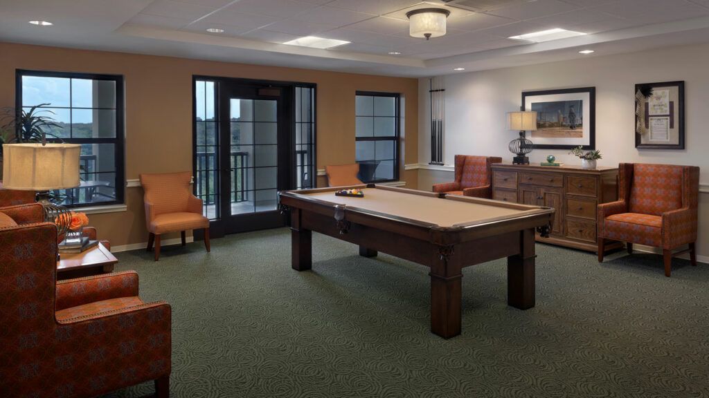 A cozy billiard room featuring a central pool table, comfortable seating, and tasteful decor.