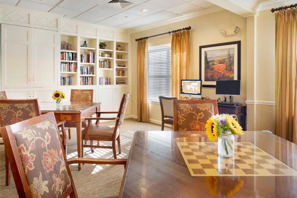 A cozy library interior with bookshelves, wooden furniture, and a vase of sunflowers.
