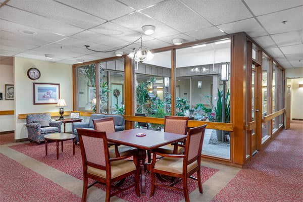 A cozy dining area with wooden furniture and glass windows overlooking an indoor garden.