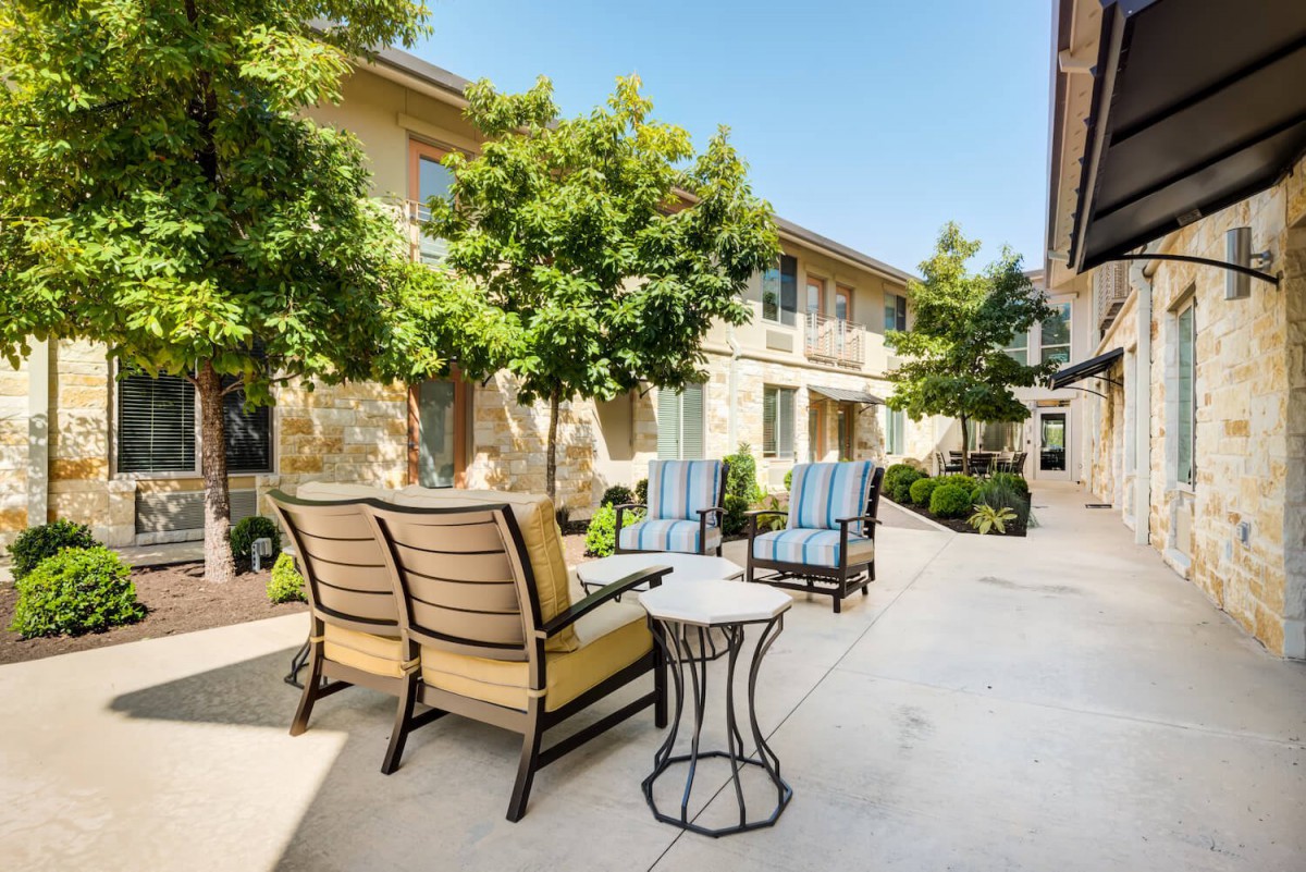A sunny courtyard with comfortable outdoor seating and lush green trees.