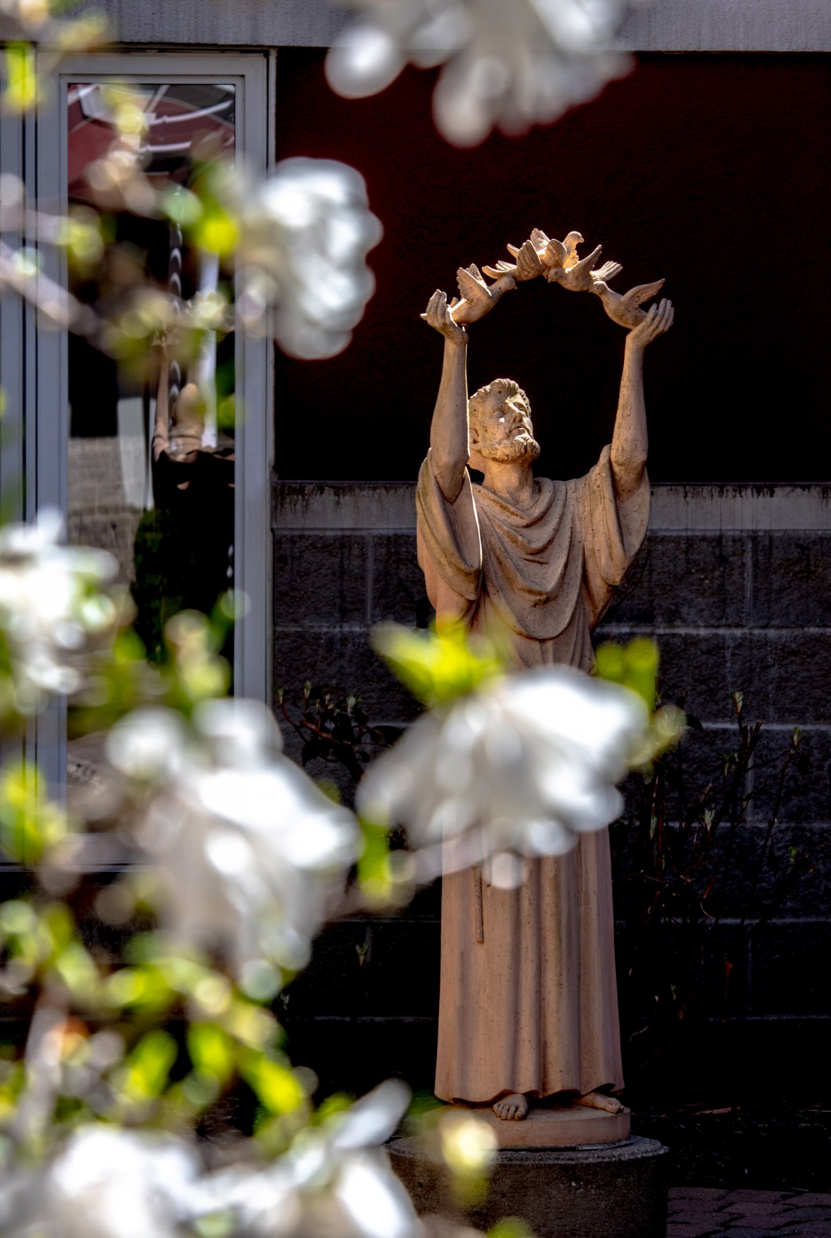 A statue holding a crown, surrounded by blooming flowers.