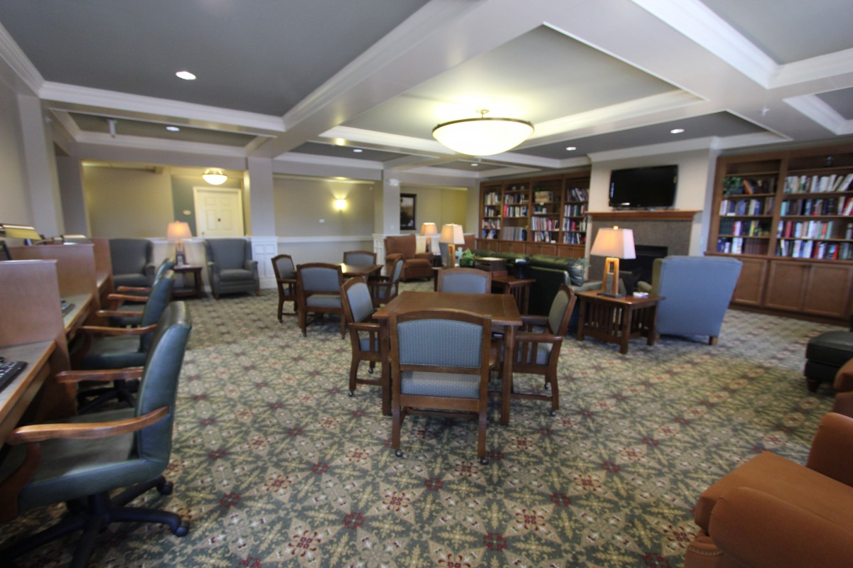 A cozy lounge area with tables and chairs, featuring bookshelves and a decorative carpet.