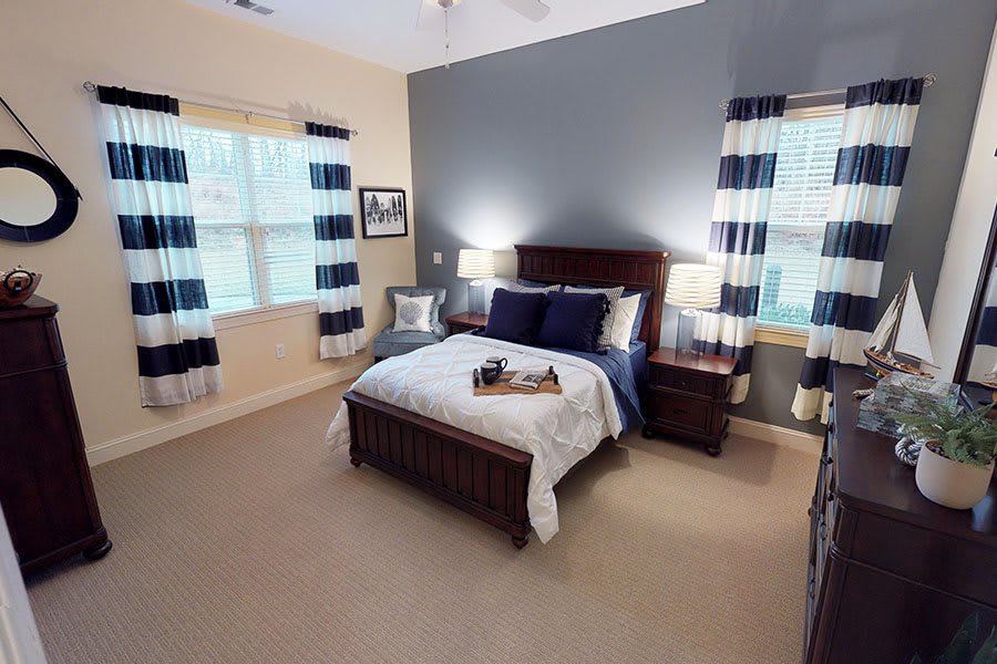 A cozy bedroom with a well-made bed, two windows with patterned curtains, and matching bedside lamps.