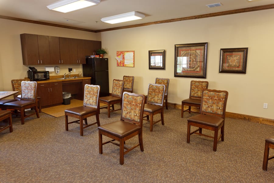 An empty meeting room with arranged chairs and kitchen area in the background.