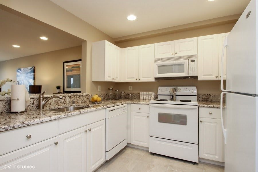 A modern kitchen with white cabinetry and granite countertops featuring an oven and microwave.