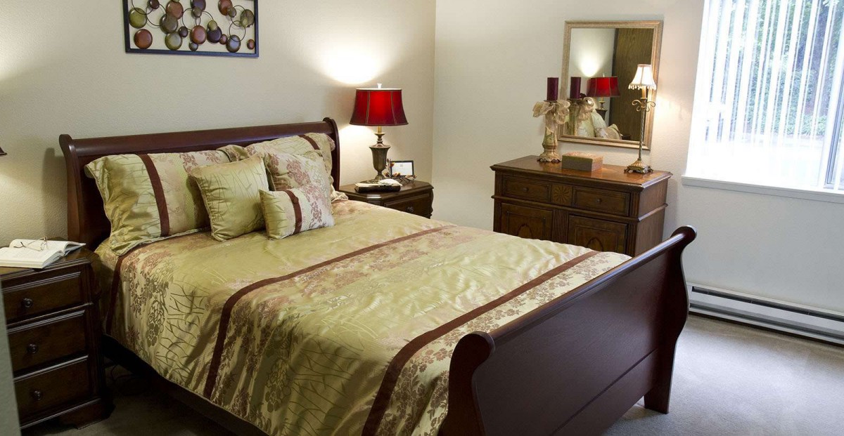 A cozy bedroom featuring a neatly made bed with decorative pillows, a wooden dresser, and a warmly lit lamp.