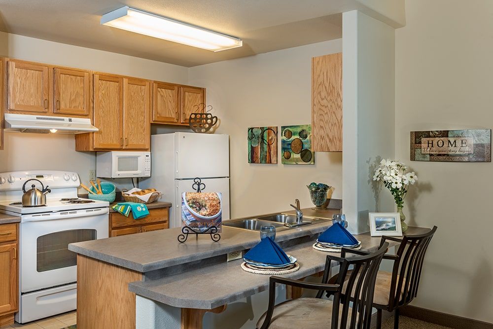A cozy kitchen with wooden cabinets, a counter with bar stools, and various decorations.