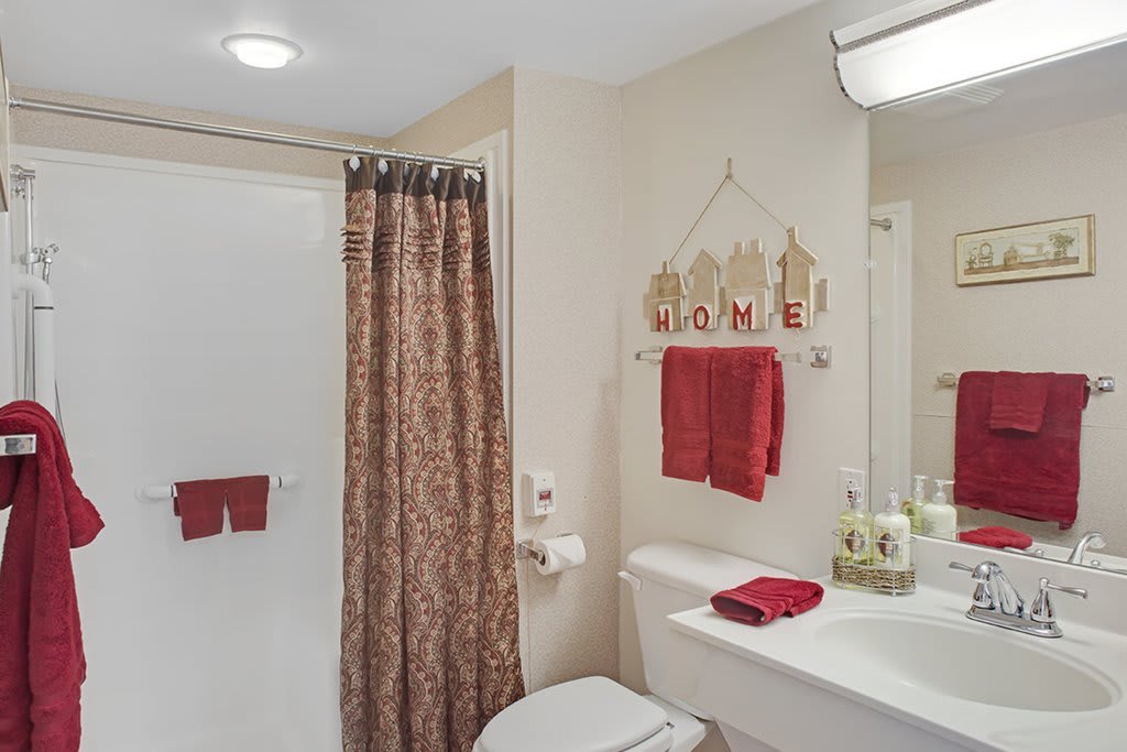 A neatly organized bathroom with red accents and decorative elements.