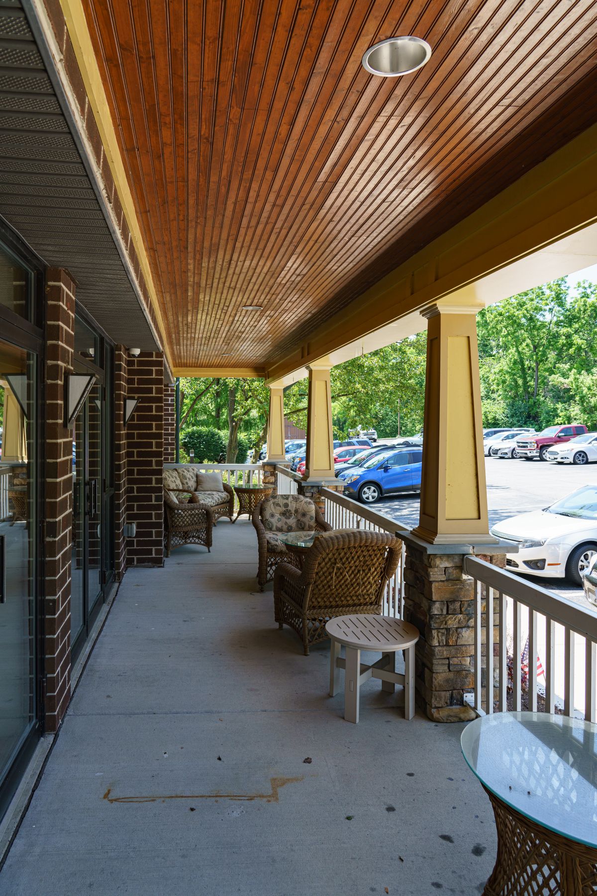 A covered porch with wicker furniture overlooking a parking lot.