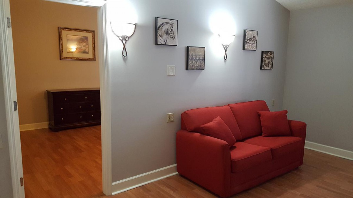 A cozy living room with a red couch and wall-mounted art pieces under warm lighting.