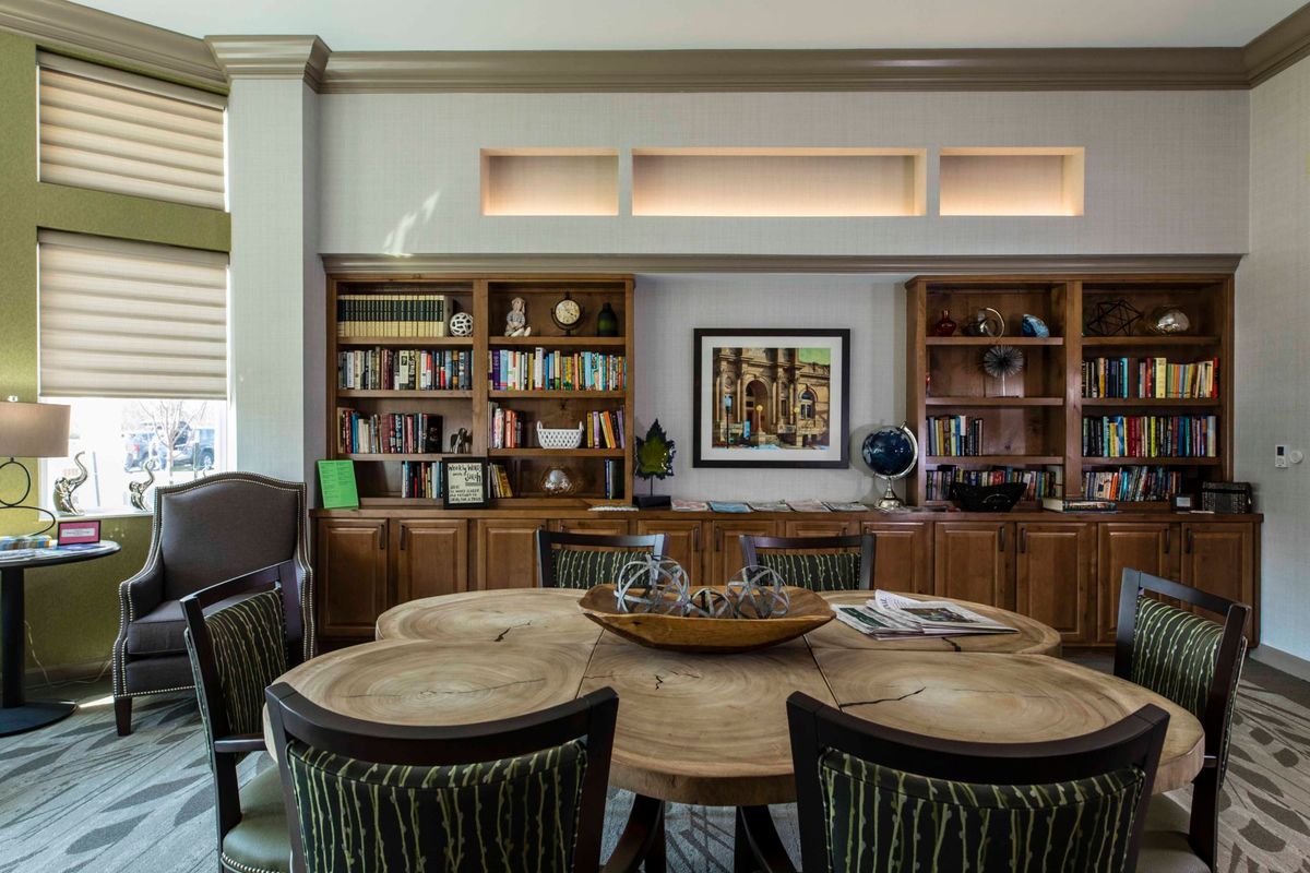 A cozy library space with wooden shelves filled with books, a round wooden table, and comfortable chairs.