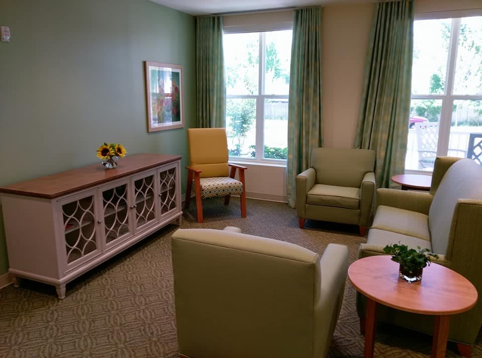 A cozy living room with comfortable chairs, a sofa, and a coffee table near a large window with green curtains.