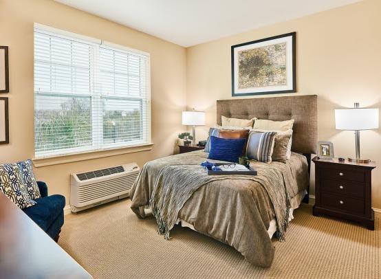 A cozy bedroom with neutral tones, featuring a neatly made bed, artwork above the headboard, and a large window letting in natural light.