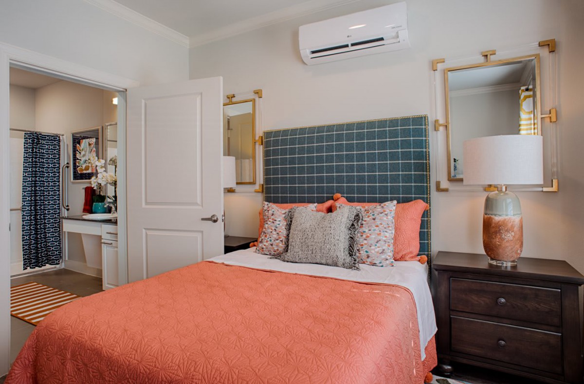 A stylishly decorated bedroom featuring a bed with orange bedding, patterned pillows, and mirrored nightstands.