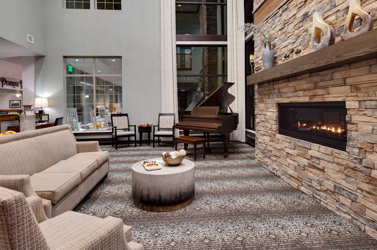 A modern living room with a grand piano, stone fireplace, and comfortable seating.