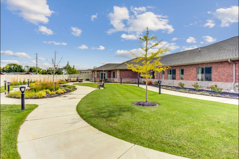 A spacious backyard features a well-maintained lawn, winding pathway, and landscaped garden under a clear blue sky.