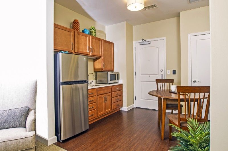 A cozy apartment kitchen with wooden cabinets, a stainless steel refrigerator, and a small dining area.