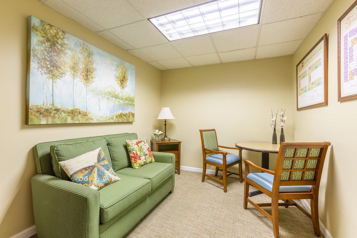 A cozy office lounge area with a green sofa, two chairs, small table, and decorative artwork on the wall.