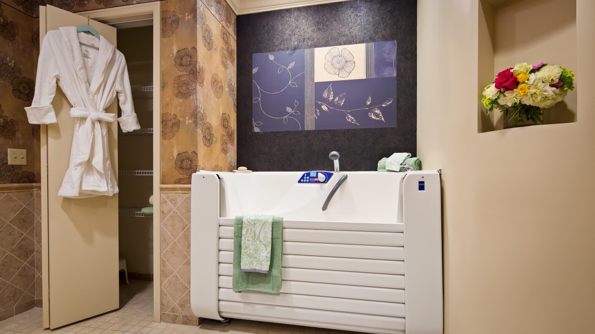 A modern bathroom featuring a white bathtub with a green towel hanging on it, set against a stylish tiled wall.