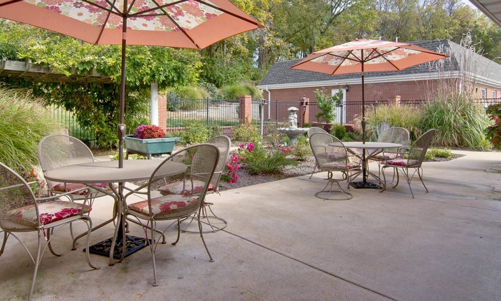 A peaceful outdoor patio with tables, chairs, and umbrellas surrounded by a garden.