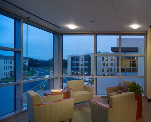 A cozy lobby area with comfortable chairs and large windows overlooking a modern building at dusk.