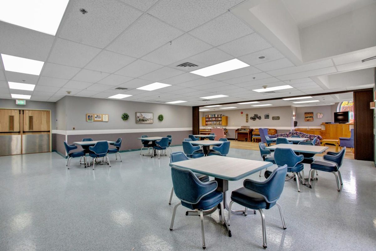 An empty cafeteria with blue chairs and white tables under fluorescent lights.