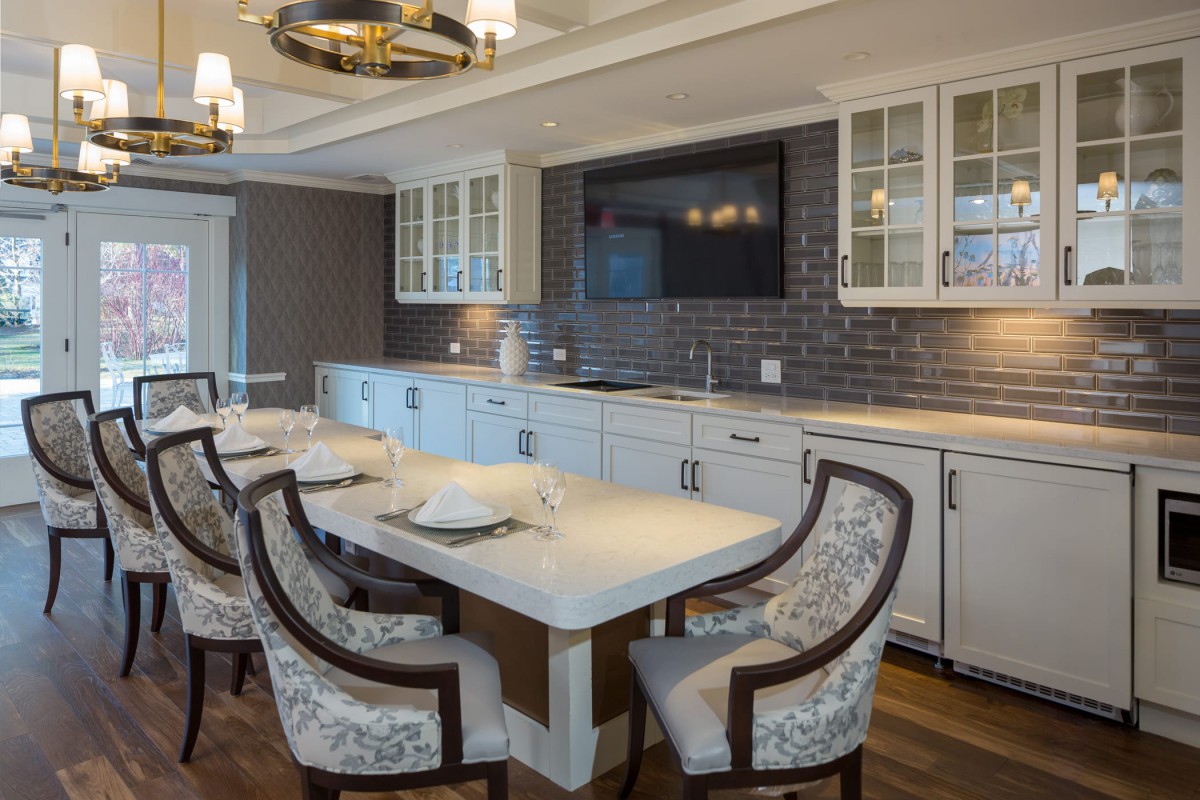 A modern kitchen with a dining area featuring white cabinets, a brick backsplash, and upholstered chairs around a dining table.