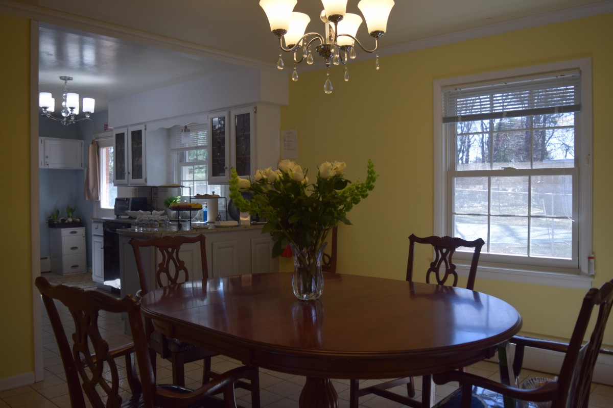A cozy dining area with a round table and a vase of flowers, adjacent to a kitchen.