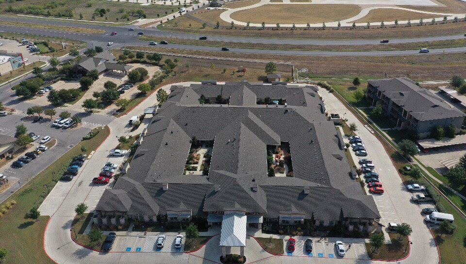 Aerial view of a large building with parking lots and a nearby highway.