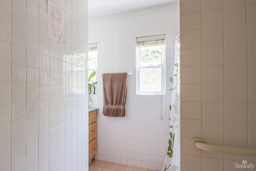 A bright and minimalist bathroom with natural light coming through the windows, featuring towels and tiled walls.