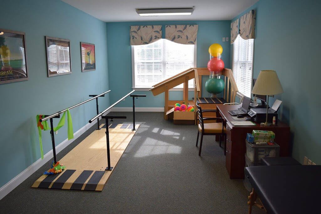 A brightly lit physical therapy room equipped with parallel bars and exercise balls.