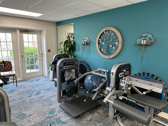 A small gym room with various exercise machines and a large wall clock.