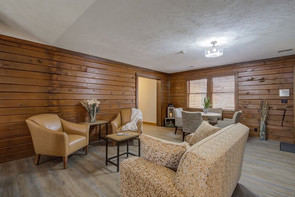 A cozy living room with wood paneling, featuring a sofa, chairs, and tables.