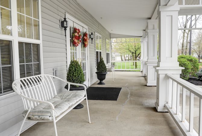 A cozy porch with a white bench, decorative plants, and festive wreaths.