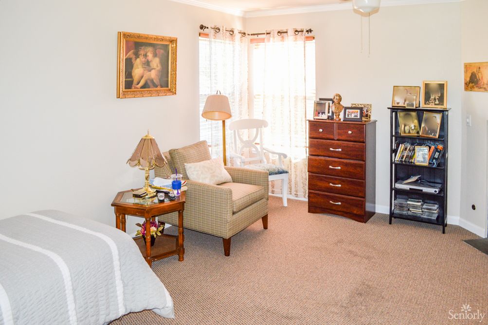 A cozy and well-lit living space featuring an armchair, a wooden dresser, and tasteful decor.