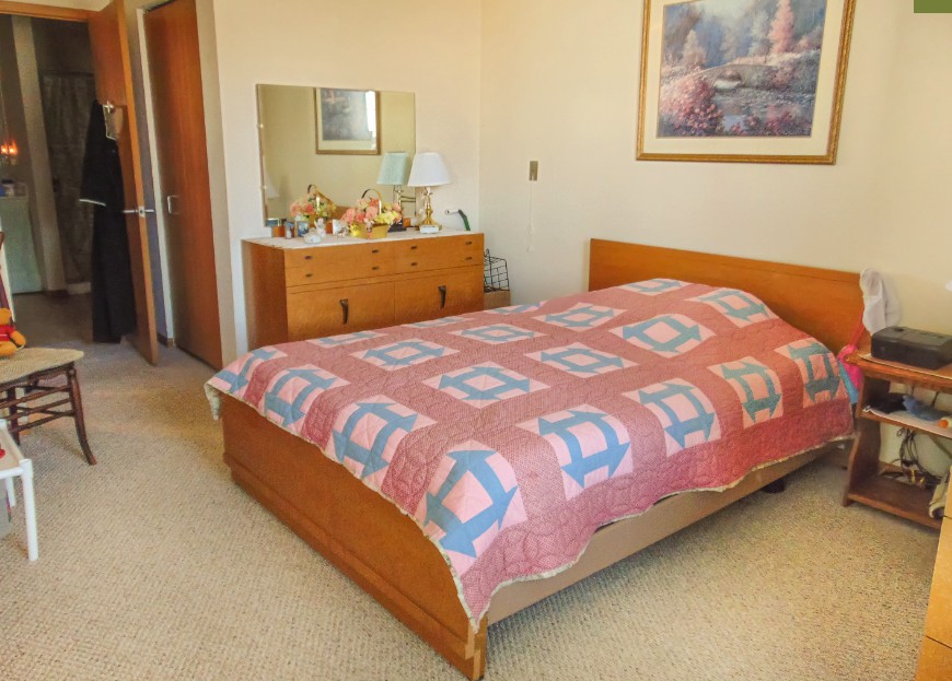 A cozy bedroom with a wooden bed adorned with a quilt, a dresser with a mirror, and framed artwork on the wall.
