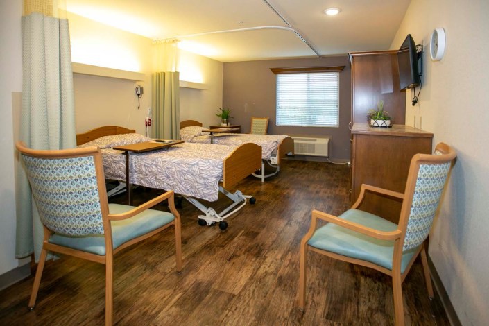 A well-lit hospital room featuring two patient beds and seating area.